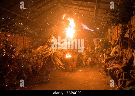 Les participants à une cérémonie des Bwiti, vêtus d'une tenue rituelle faite de feuilles de palmier séchées, dansent avec des torches allumées à l'intérieur d'un petit temple. Banque D'Images