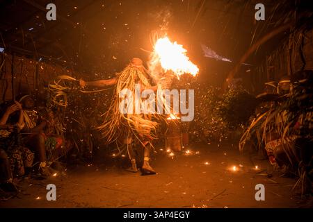 Les participants à une cérémonie des Bwiti, vêtus d'une tenue rituelle faite de feuilles de palmier séchées, dansent avec des torches allumées à l'intérieur d'un petit temple. Banque D'Images