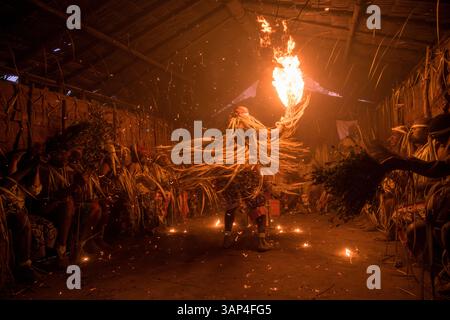 Les participants à une cérémonie des Bwiti, vêtus d'une tenue rituelle faite de feuilles de palmier séchées, dansent avec des torches allumées à l'intérieur d'un petit temple. Banque D'Images