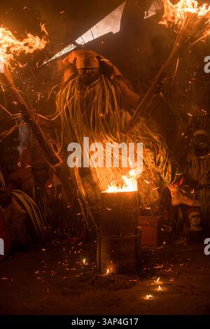 Les participants à une cérémonie des Bwiti, vêtus d'une tenue rituelle faite de feuilles de palmier séchées, dansent avec des torches allumées à l'intérieur d'un petit temple. Banque D'Images
