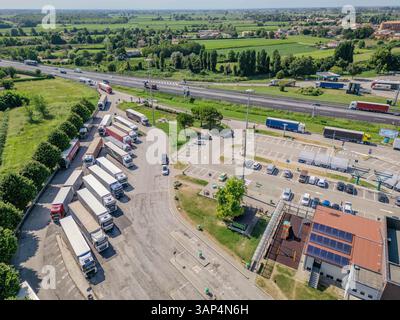 Vue aérienne d'une station-service très fréquentée et autoroute avec camions garés, Cessalto, Italie. Banque D'Images