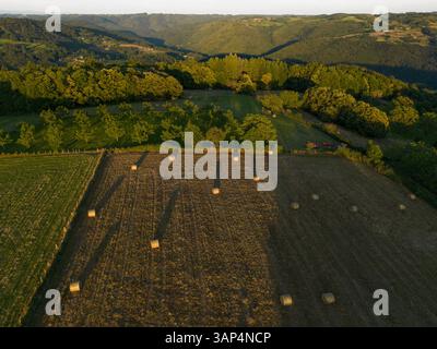 Vue aérienne de belles terres agricoles pastorales avec collines ondulantes et balles de foin au coucher du soleil, Chenailler-Mascheix, France. Banque D'Images