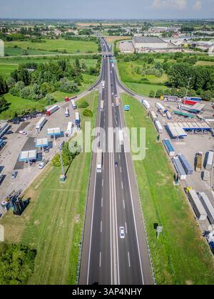 Vue aérienne d'une autoroute très fréquentée avec des camions et une station d'essence entourée d'une belle campagne, Cessalto, Italie. Banque D'Images