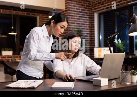 Deux femmes professionnelles dans une réunion de bureau tard le soir, comparant des notes et analysant des documents. Des collègues multiethniques élaborent des stratégies pour un projet d'entreprise et prennent des décisions importantes ensemble. Banque D'Images