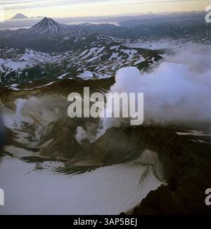 Vue aérienne d'une majestueuse montagne volcanique enneigée avec de la fumée qui monte, Kamtchatka, Russie. Banque D'Images