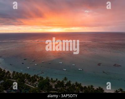 Vue aérienne du coucher de soleil tranquille sur l'océan avec littoral pittoresque, palmiers et bateaux, rivière Noire, Maurice. Banque D'Images