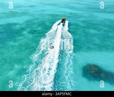 Vue aérienne des gens profitant d'un funtube derrière un bateau sur l'eau turquoise et les coraux vibrants, Vashafaru, Haa Alif, Maldives. Banque D'Images