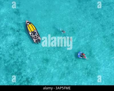 Vue aérienne de personnes pratiquant des sports nautiques sur un funtube derrière un bateau dans une eau turquoise claire avec de beaux coraux, Vashafaru, Haa Alif, Maldives. Banque D'Images
