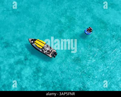 Vue aérienne des gens profitant d'un funtube derrière un bateau sur des eaux turquoises claires avec des coraux vibrants, Vashafaru, Haa Alif, Maldives. Banque D'Images