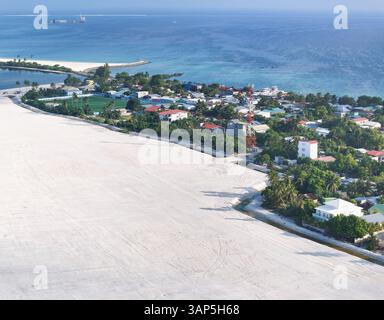 Vue aérienne de la zone de récupération avec des maisons et des palmiers le long de la côte et l'océan bleu, Maradhoo, Maldives. Banque D'Images