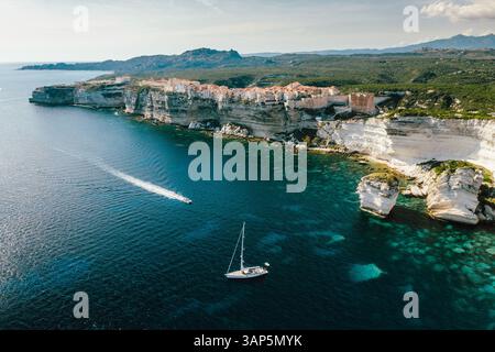 Vue aérienne d'un voilier ancré avec un speed boat passant devant Bonifacio, Corse, France. Banque D'Images