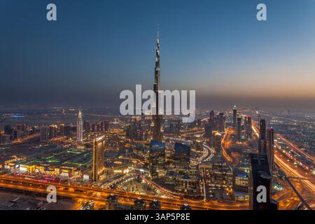 Vue aérienne du Burj Khalifa illuminé surplombant un paysage urbain moderne la nuit, Dubaï, Émirats arabes Unis. Banque D'Images