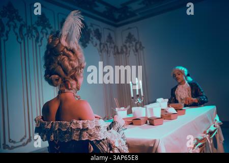 Élégant couple dans des costumes historiques profite d'un dîner fusion unique sous la lumière bleue ambiante néon Banque D'Images