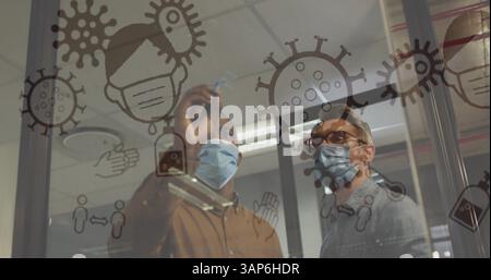 Image des cellules et icônes covid 19 flottant au-dessus de deux hommes dans des masques faciaux au bureau Banque D'Images