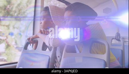 Image d'un faisceau de lumière bleue au-dessus de deux afro-américaines dans le bus regardant par la fenêtre Banque D'Images