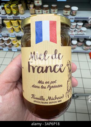 Main tenant un pot de miel famille Michaud, produit en France, dans une allée de supermarché - FORBACH, FRANCE - 12 AVRIL 2025 Banque D'Images