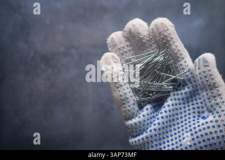 Main tenant plusieurs clous métalliques sur un fond sombre Banque D'Images