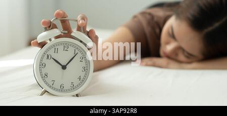 Paresseux Asie jeune femme ferme un réveil, dame est rendez-vous tardif ou travail ou étude de classe, surdormi, difficulté à se lever le matin, le temps inquiet, non Banque D'Images