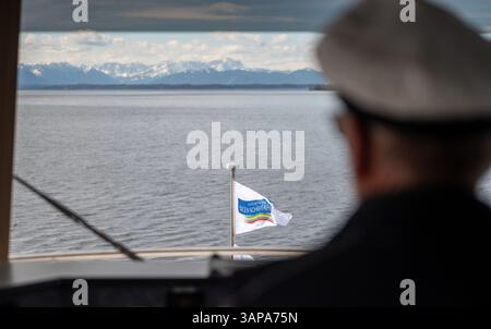 Starnberg, Allemagne. 16 avril 2025. Un drapeau portant l'inscription 'Bayerische Seen-Schiffahrt' (navigation sur les lacs bavarois) flotte sur un bateau d'excursion naviguant sur le lac de Starnberg devant le panorama montagneux des Alpes bavaroises enneigées. Crédit : Leonie Asendorpf/dpa/Alamy Live News Banque D'Images
