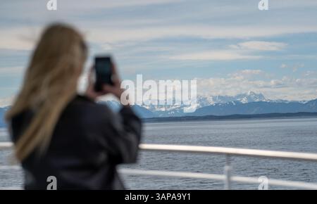 Starnberg, Allemagne. 16 avril 2025. Une jeune femme naviguant sur le lac de Starnberg sur un bateau d'excursion prend une photo des Alpes bavaroises enneigées avec son smartphone. Crédit : Leonie Asendorpf/dpa/Alamy Live News Banque D'Images