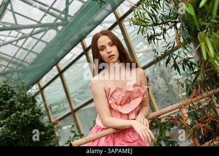 Une jeune femme respire la beauté et la grâce dans une serre ensoleillée de verdure luxuriante. Banque D'Images
