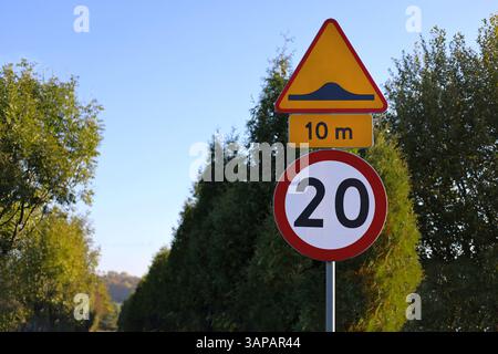 panneau routier de limitation de vitesse de 20 kilomètres par heure avec panneau d'avertissement de bosses de vitesse. Arbres flous et fond de ciel. Banque D'Images