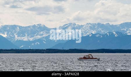 Starnberg, Allemagne. 16 avril 2025. Un petit bateau à moteur navigue sur le lac de Starnberg avec pour toile de fond les Alpes bavaroises enneigées. Crédit : Leonie Asendorpf/dpa/Alamy Live News Banque D'Images