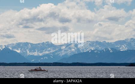 Starnberg, Allemagne. 16 avril 2025. Un petit bateau à moteur navigue sur le lac de Starnberg avec pour toile de fond les Alpes bavaroises enneigées. Crédit : Leonie Asendorpf/dpa/Alamy Live News Banque D'Images
