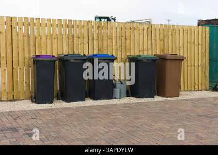 Rangée de bacs de recyclage de déchets domestiques en plastique à code de couleur sur les dalles de pavage devant la nouvelle clôture de jardin en bois dans le quartier résidentiel Banque D'Images