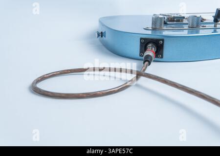 Une guitare électrique bleue avec un câble audio branché dans sa prise d'entrée, isolée sur un fond blanc propre. Banque D'Images