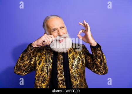 Homme barbu excentrique en veste dorée faisant des gestes en toute confiance sur un fond violet éclatant Banque D'Images