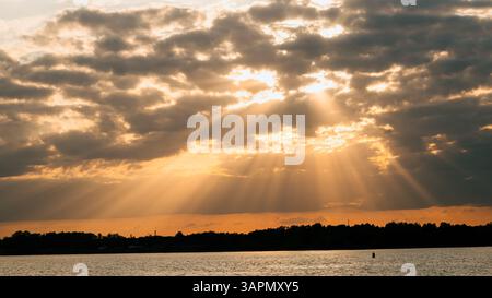 Des rayons de soleil dorés spectaculaires qui brillent à travers les nuages sombres créent un coucher de soleil à couper le souffle sur un lac tranquille, illuminant le paysage serein et reflétant la beauté de la surface de l'eau Banque D'Images