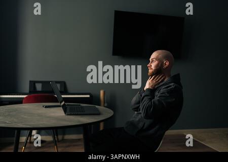 Freelance fatiguée touchant le cou tout en étant assise au bureau à domicile avec ordinateur portable, regardant pensif et contemplatif après une longue journée de travail. Banque D'Images