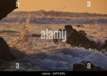 Coucher de soleil sur l'océan Pacifique avec des vagues s'écrasant contre les rochers côtiers, capturant la beauté brute et l'énergie du littoral Banque D'Images