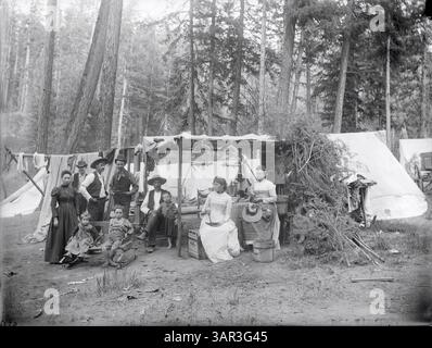 Cette photographie en noir et blanc montre quatre hommes, trois femmes et trois enfants posés devant un camping avec divers équipements de camping, offrant un aperçu de la vie en plein air du XIXe siècle et des voyages en Amérique. Banque D'Images