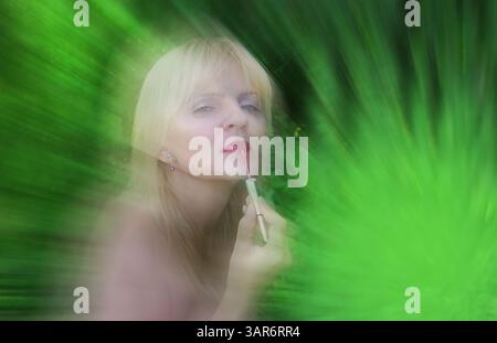 Fond vert avec une femme mature blonde floue appliquant de la crème de rouge à lèvres sur ses lèvres Banque D'Images