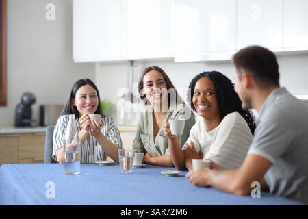 Quatre amis interraciaux parlant et buvant du café dans la cuisine à la maison Banque D'Images