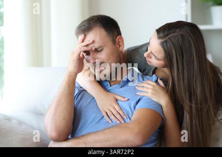 Homme triste réconforté par une femme assise sur un canapé à la maison Banque D'Images