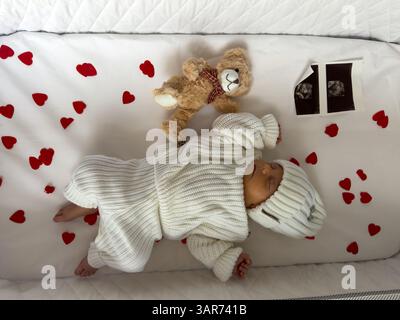 Bébé nouveau-né dormant dans un berceau avec des coeurs et un ours en peluche Banque D'Images