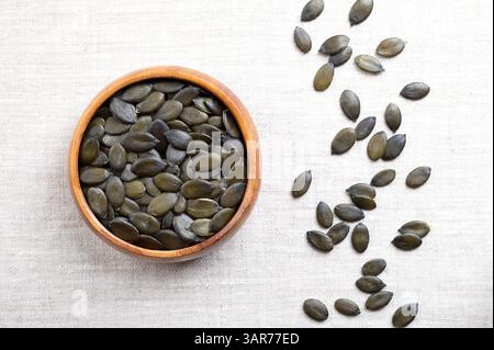 Graines de citrouille à l'huile de Styrie dans un bol en bois sur lin. Fruits séchés, vert foncé et jeunes de la citrouille styrienne, Cucurbita pepo var. styriaca. Banque D'Images