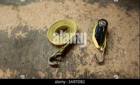 Sangles à cliquet jaunes avec métal et crochets en S disposés sur un sol en béton, utilisées pour arrimer les cargaisons Banque D'Images