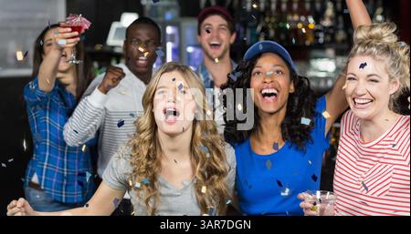 Image de confettis tombant sur un groupe diversifié heureux d'amis buvant dans le bar Banque D'Images