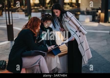 Trois femmes collaborant à l'extérieur tout en examinant des documents sur un banc de rue Banque D'Images