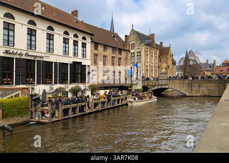 Le bateau touristique part d'un débarquement sur un canal de Bruges, en passant devant des bâtiments historiques et un pont de pierre bondé de Onlook Banque D'Images