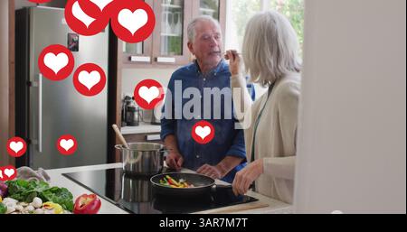 Image d'icônes de cœur de médias sociaux sur un couple senior cuisinant dans la cuisine Banque D'Images