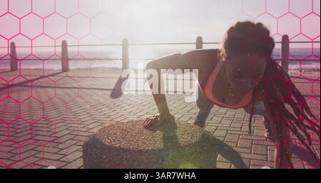 Formes hexagonales roses contre t african american fit femme effectuant des pompes sur la promenade Banque D'Images
