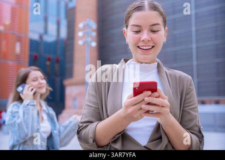 Jeunes femmes caucasiennes utilisant des smartphones dans un environnement urbain moderne Banque D'Images