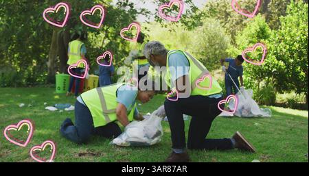 Image de cœurs se déplaçant au-dessus d'une famille afro-américaine heureuse ramassant des ordures dans la campagne Banque D'Images