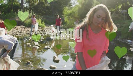 Image de cœurs verts sur divers groupes heureux ramassant des ordures dans la campagne Banque D'Images