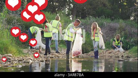 Image de cœurs rouges sur un groupe diversifié ramassant des ordures par la rivière dans la campagne Banque D'Images
